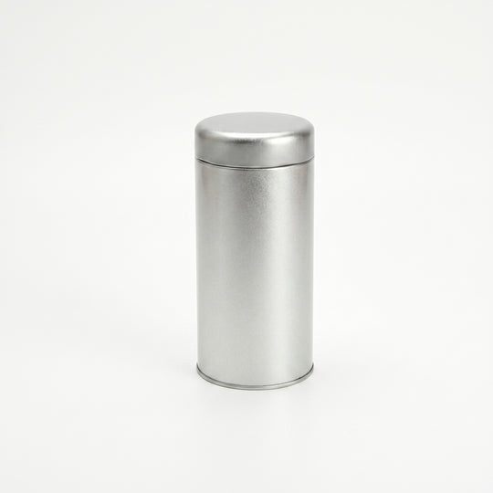 Round silver tea tin with slip lid standing upright on white background.