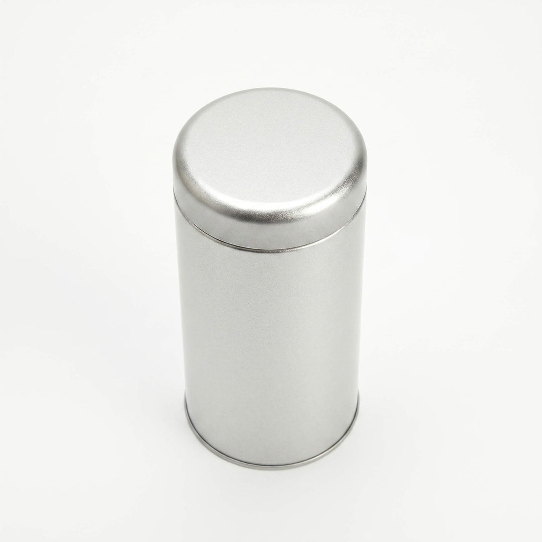 Round silver metal tea tin with fitted slip lid viewed from top angle on white background.